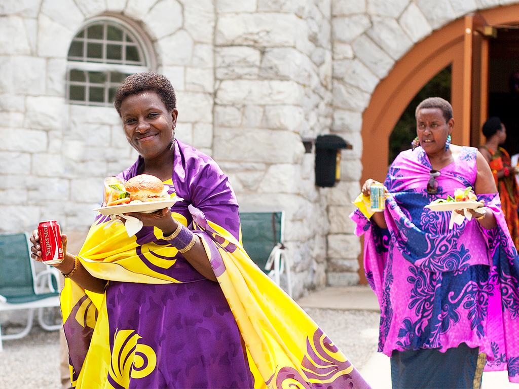 CDE_FoodBurgers_Horizontal 2 women in colorful attire are carrying plates of food outside of the CDE building